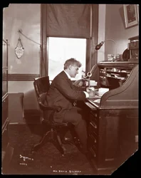David Belasco schreibt an einem Schreibtisch in den Büros seines Theaters, 1902